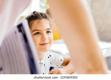 Smiling Caucasian With Unrecognizable Female Teacher Teaching Nice American Elementary Girl At Desk In Classroom. Education And School Concept.