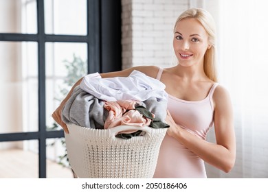 Smiling caucasian woman carrying laundry basket at home.Housewife using washing machine for dirty clothes.