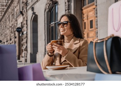 Smiling caucasian woman girl in sunglasses having coffee tea hot beverage on the street sitting in cafe after shopping, relaxing resting alone. - Powered by Shutterstock