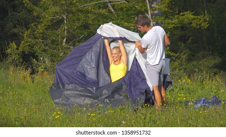 Smiling Caucasian woman having fun while pitching a tent next to the calm forest with her boyfriend. Carefree tourist couple working together to set up a tent and campsite during summer journey. - Powered by Shutterstock