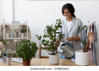 Smiling Caucasian woman hold pot can watering green plant in office workplace. Happy millennial female gardener or florist take care of domestic flowers, enrich cultivate ground. Gardening concept. - Powered by Shutterstock