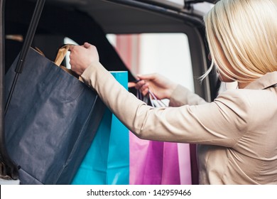 Smiling Caucasian Woman Putting Her Shopping Bags Into The Car Trunk.