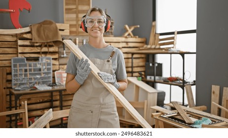 Smiling caucasian woman in safety goggles holding lumber at a carpentry workshop - Powered by Shutterstock