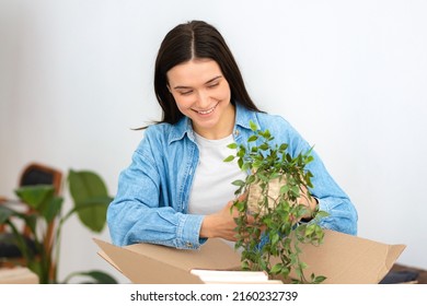 Smiling Caucasian Woman Unpacking Boxes In Her New Home Or In A Student Dorm Room. Moving To A New House, Rent