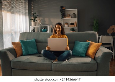 Smiling caucasian woman using laptop while sitting on couch at home. Happy female having a video call or online meeting with a client or colleagues from work. - Powered by Shutterstock