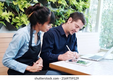 Smiling Caucasian Young barista couple love or partnership is wearing apron and consulting for marketing planning idea with tablet in the coffee shop. Start up for small cafe business owner concept.  - Shutterstock ID 2169759129