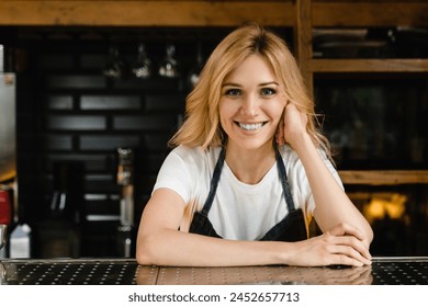 Smiling caucasian young waitress small business owner barista bartender in blue apron looking at the camera standing at the bar restaurant counter - Powered by Shutterstock