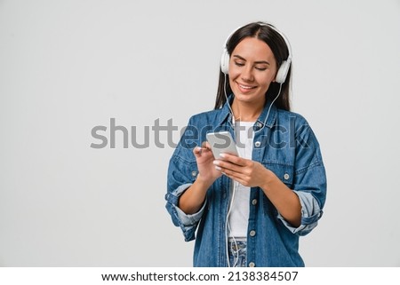Smiling caucasian young woman listening to the podcast e-book music song singer rock band in headphones earphones, choosing sound track on cellphone isolated in white background