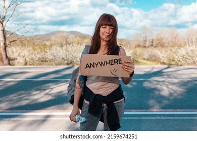 Smiling caucasian young woman with tattoed hand holding a cardboard sign with text anywhere. The concept of local traveling and hitchhiking.