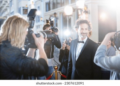 Smiling celebrity in tuxedo being photographed by paparazzi at red carpet event - Shutterstock ID 2307612091