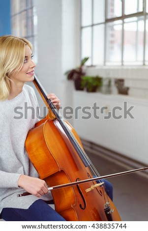 Smiling cellist holding her instrument and bow stares towards the window while seated in her living room