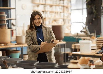 Smiling ceramics studio owner doing inventory in a pottery workshop - Powered by Shutterstock