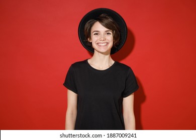 Smiling cheerful beautiful attractive young brunette woman 20s years old wearing casual basic black t-shirt hat standing and looking camera isolated on bright red color background studio portrait - Powered by Shutterstock