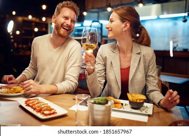 Smiling cheerful couple sitting in a restaurant, having dinner and chatting. Man talking to a woman while a woman listening to him and drinking white wine. - Powered by Shutterstock