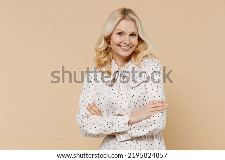 Smiling cheerful elderly gray-haired blonde woman lady 40s years old wears pink dress hold hands crossed isolated on plain pastel beige background studio portrait. People emotions lifestyle concept