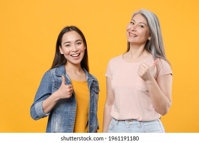 Smiling Cheerful Family Two Asian Women Girls Gray-haired Mother And Brunette Daughter In Casual Clothes Posing Showing Thumbs Up Looking Camera Isolated On Yellow Color Background Studio Portrait