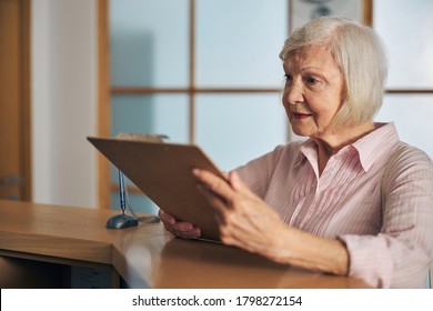 Smiling Cheerful Female Looking At The Price List In Medical Clinic While Standing Near The Front Desk