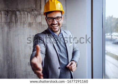 Smiling cheerful friendly constructor in suit and with helmet on head introducing himself.