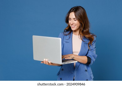 Lächelnd fröhlich lustige schöne junge Brunette Frau 20er mit einfachem, lockeren Jackett, die auf Laptop PC-Computer arbeitet einzeln auf hellblauem Hintergrund Studioportrait