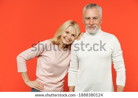 Smiling cheerful funny couple two friends elderly gray-haired man blonde woman wearing white pink casual clothes standing looking camera isolated on bright orange color background studio portrait