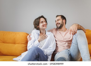 Smiling cheerful funny laughing young couple two friends man woman 20s wearing casual clothes sitting on couch hugging looking at each other resting relaxing spending time in living room at home
