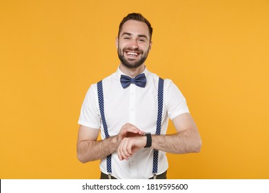 Smiling Cheerful Funny Young Bearded Man 20s Wearing White Shirt Bow-tie Suspender Posing Standing Wearing Smart Watch On Hand Isolated On Bright Yellow Color Wall Background Studio Portrait