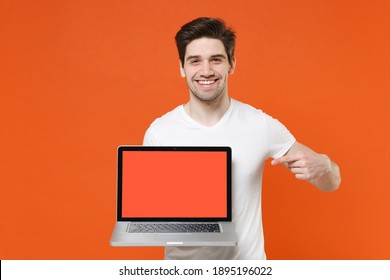Smiling Cheerful Funny Young Man 20s Wearing Basic Casual White T-shirt Pointing Index Finger On Laptop Pc Computer With Blank Empty Screen Isolated On Bright Orange Colour Background Studio Portrait