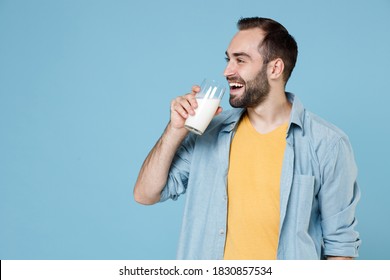 Smiling cheerful handsome young bearded man 20s wearing casual clothes posing holding in hand glass drinking vegan milk looking aside isolated on pastel blue color wall background studio portrait