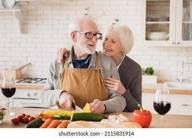 Smiling cheerful happy caucasian senior old elderly couple family grandparents spouses wife and husband cooking together, helping make vegetable vegan vegetarian salad at home kitchen