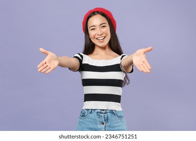 Smiling cheerful happy joyful young brunette asian woman wearing striped t-shirt red beret standing reach out stretch hands looking camera isolated on pastel violet colour background studio portrait - Powered by Shutterstock