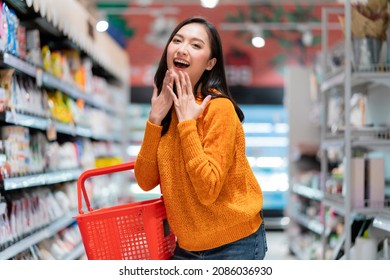 Smiling Cheerful And Joyful Female Woman Hand Hold Shopping Basket Hand Gesture Greeting Surprise Standing Between Supermarket Product Shelf Aisel Convenience Store Supermarket Department Store Mall