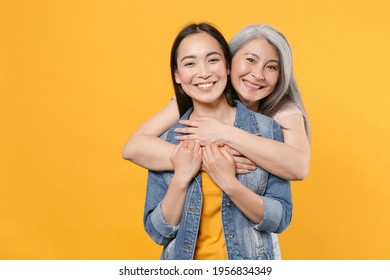 Smiling Cheerful Pretty Family Asian Female Women Girls Gray-haired Mother And Brunette Daughter In Casual Clothes Posing Hugging Looking Camera Isolated On Yellow Color Background Studio Portrait