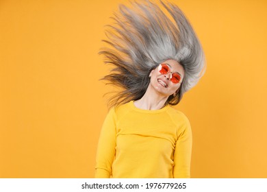 Smiling cheerful pretty gray-haired asian woman in casual clothes eyeglasses dancing jumping with fluttering hair having fun looking camera isolated on bright yellow colour background studio portrait