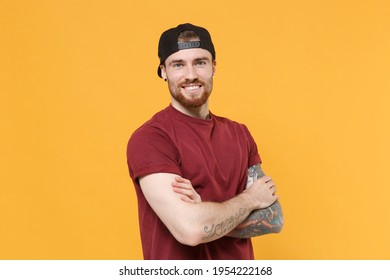 Smiling cheerful young bearded tattooed man in casual t-shirt, black cap holding hands crossed folded isolated on yellow background studio portrait. Mock up copy space. Tattoo translate life is fight