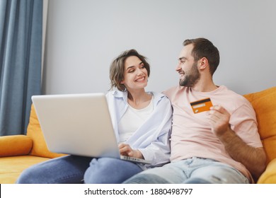 Smiling Cheerful Young Couple Man Woman 20s Family Husband Wife In Casual Clothes Sitting On Couch Using Laptop Pc Computer Hold Credit Bank Card Resting Relaxing Spending Time In Living Room At Home