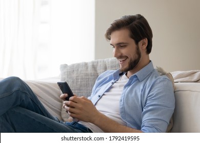 Smiling cheerful young man using smartphone, laughing handsome guy surfing internet, watching funny video, chatting or shopping online, looking at phone screen, browsing mobile device apps