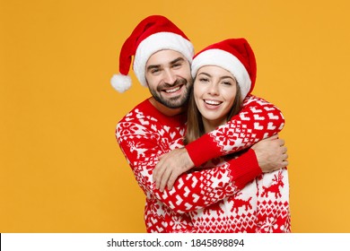 Smiling Cheerful Young Santa Couple Friends Man Woman 20s Wearing Red Sweater Christmas Hat Hugging Isolated On Yellow Background Studio Portrait. Happy New Year Celebration Merry Holiday Concept