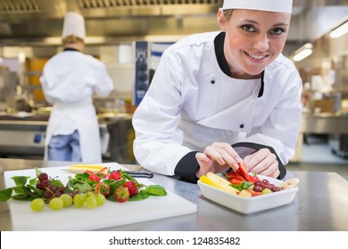 Smiling chef putting a strawberry in the fruit bowl in the kitchen