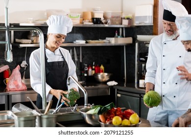 Smiling chef washing broccoli near interracial colleagues talking in restaurant kitchen - Powered by Shutterstock