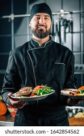 Smiling Chef, Wearing Black Uniform, Serving Organic Vegan Burger With Fresh Salad