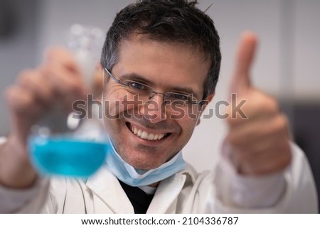 Smiling chemist with blue solution in hand. Research and satisfaction concept
