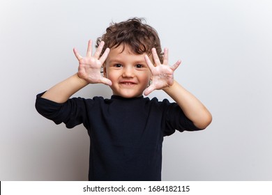 Smiling Child, A Boy In A Black T-shirt Shows His Hands In Soapy Water On A White Studio Background. Hand Disinfection. Soaped Palms And Fingers