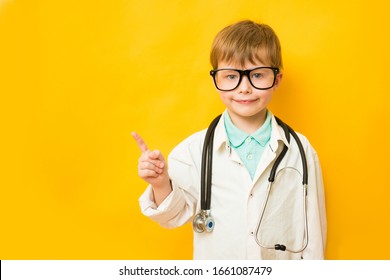 Smiling Child Boy Doctor On Yellow Background. Male Doc In White Medical Gown Pointing Index Finger Aside. Healthcare Health Medicine Concept. Mock Up Copy Space