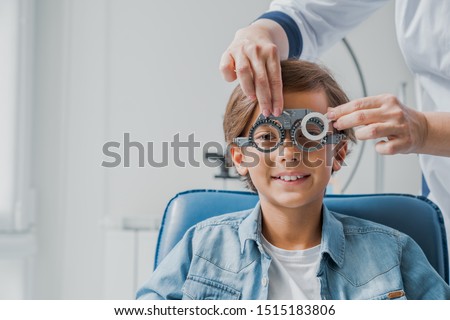 Smiling child boy in glasses checks eye vision at pediatric ophthalmologist