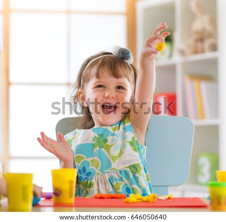 Smiling child girl is learning to use colorful play dough in a well lit room near window