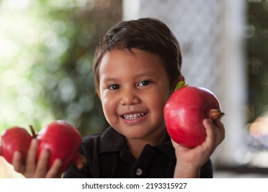 Smiling Child Holding Up In His Little Hands Some Freshly Cut Pomegranates That Are Grown Organically.