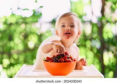 Smiling Child Reaches For Fruit In Bowl On Table