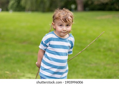 Smiling child with sweaty hairs holding sticks and playing in the park in summer hot weather. Looking at the camera