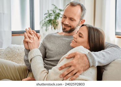 smiling child-free couple holding hands and embracing on couch in living room, warm relationship - Powered by Shutterstock