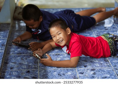  Smiling children in good spirits, two men, brothers, lying down playing games from smartphones and tablets. - Powered by Shutterstock